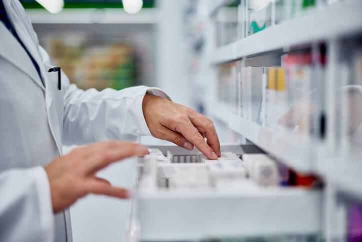 A pharmacy assistant is organizing medication inventory on pharmacy shelves